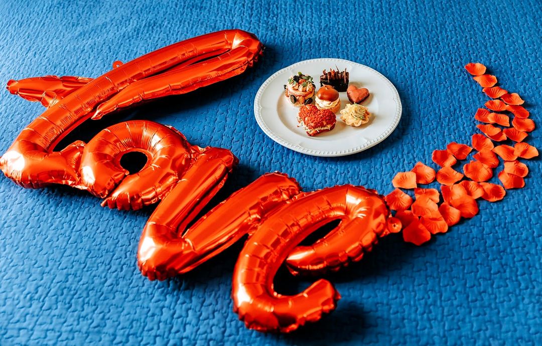 A creative food presentation featuring red foil balloons arranged as a lobster design with appetizers on a white plate against a blue textured background.